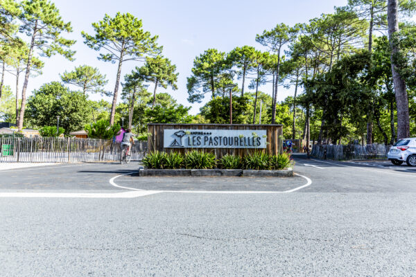 Entrée du camping Les Pastourelles avec panneau enseigne et pins maritimes